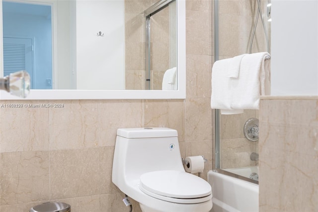 bathroom featuring tile walls, enclosed tub / shower combo, and toilet