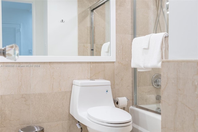bathroom with tile walls, toilet, and bath / shower combo with glass door