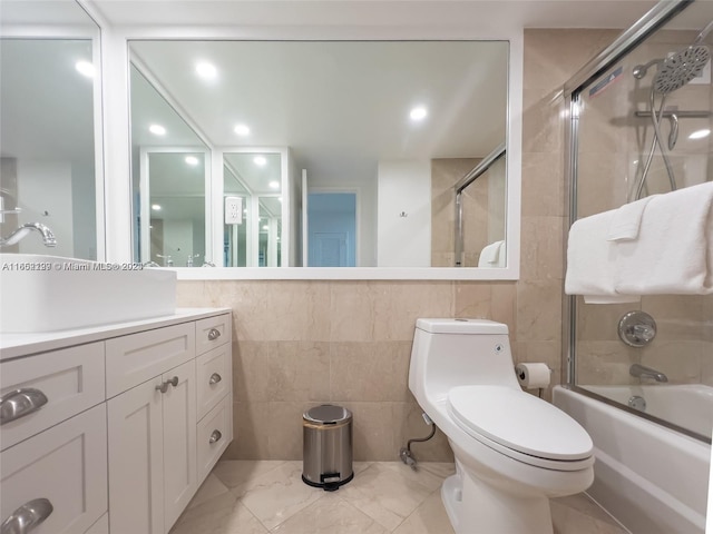 full bathroom featuring tile walls, toilet, bath / shower combo with glass door, and vanity