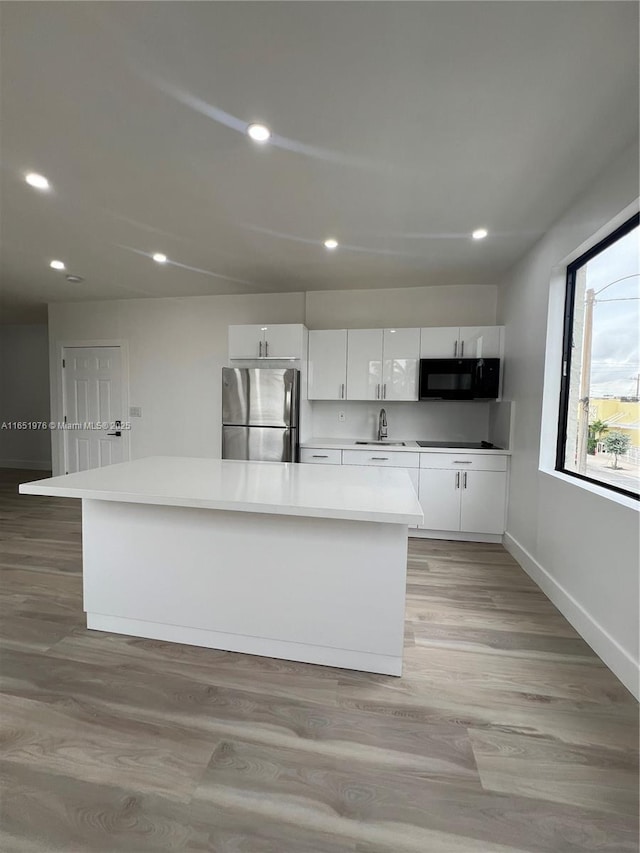 kitchen with white cabinets, sink, light wood-type flooring, a kitchen island, and stainless steel refrigerator