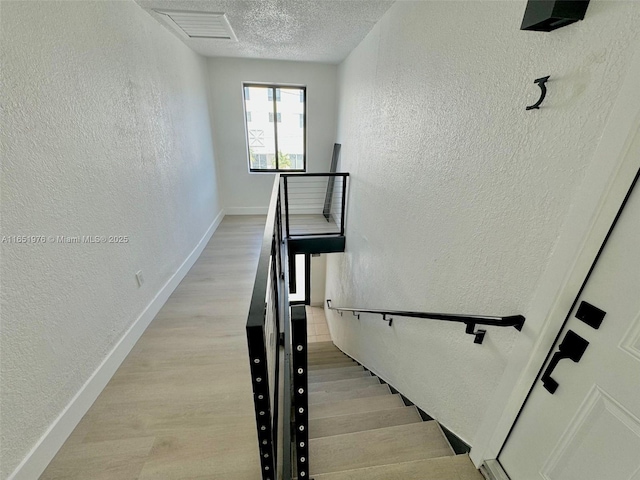 staircase with a textured ceiling and hardwood / wood-style flooring