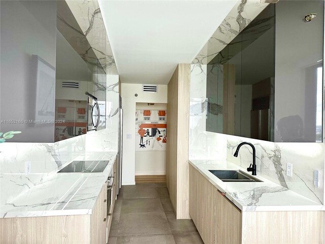 kitchen with backsplash, light stone countertops, sink, light brown cabinets, and black electric stovetop