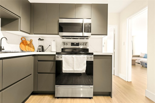 kitchen featuring stainless steel appliances, gray cabinetry, and light wood-type flooring