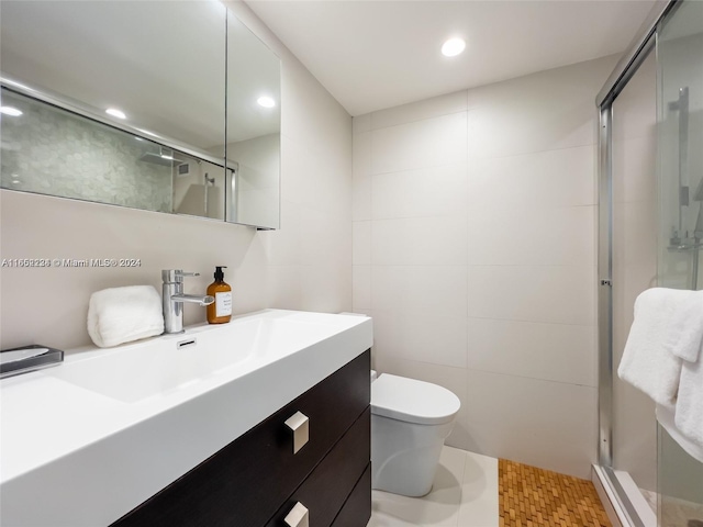 bathroom with a shower with door, vanity, tile walls, toilet, and tile patterned floors