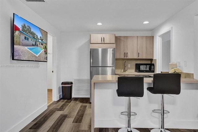 kitchen with dark hardwood / wood-style floors, tasteful backsplash, a breakfast bar, stainless steel refrigerator, and light brown cabinets