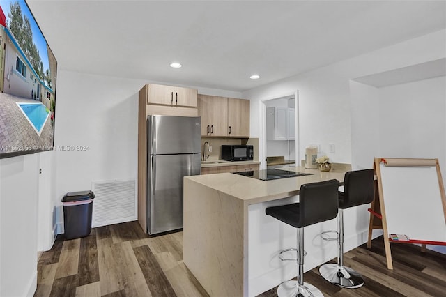 kitchen featuring black appliances, dark wood-type flooring, kitchen peninsula, sink, and light brown cabinets