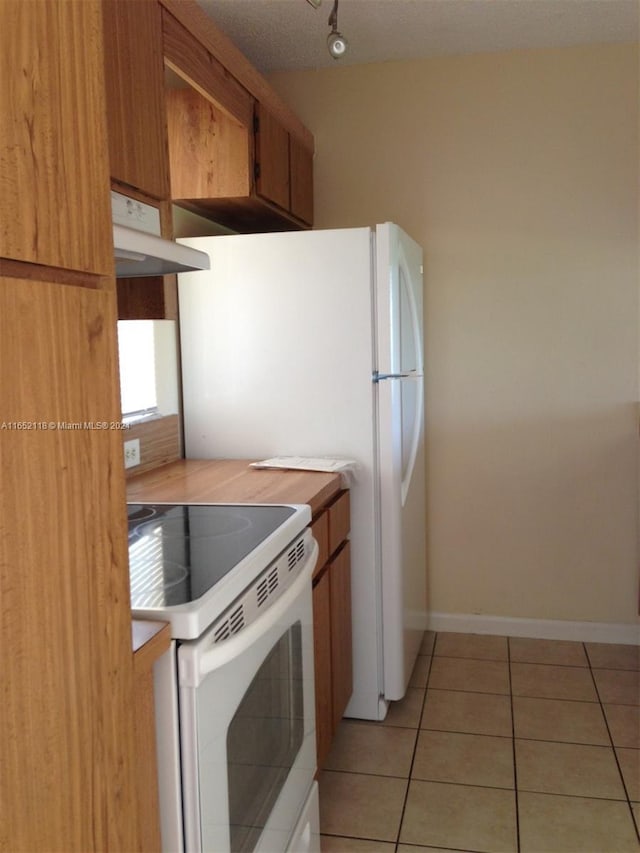 kitchen with electric range, under cabinet range hood, light tile patterned flooring, light countertops, and baseboards