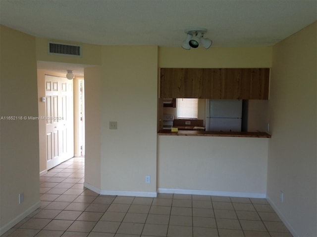 kitchen with stove, white fridge, light tile patterned floors, and kitchen peninsula