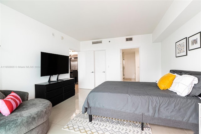 bedroom featuring light tile patterned flooring, visible vents, ensuite bath, and a closet