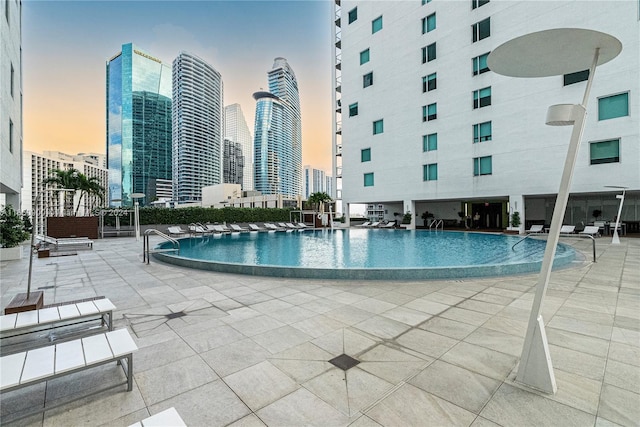 pool at dusk with a view of city, a community pool, and a patio