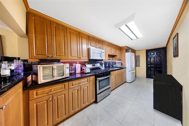 kitchen featuring white appliances, light tile patterned floors, crown molding, sink, and dark stone counters