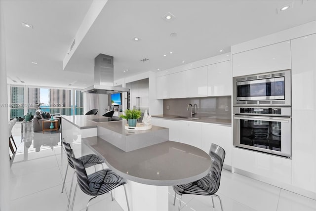 kitchen featuring white cabinets, appliances with stainless steel finishes, a breakfast bar area, and island range hood