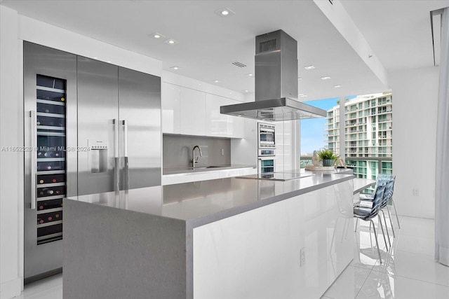 kitchen featuring white cabinetry, built in appliances, a kitchen bar, a center island, and island exhaust hood