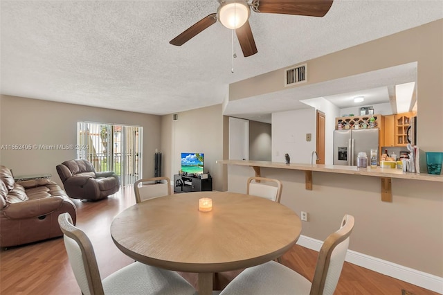 dining room with light wood-type flooring, ceiling fan, and a textured ceiling