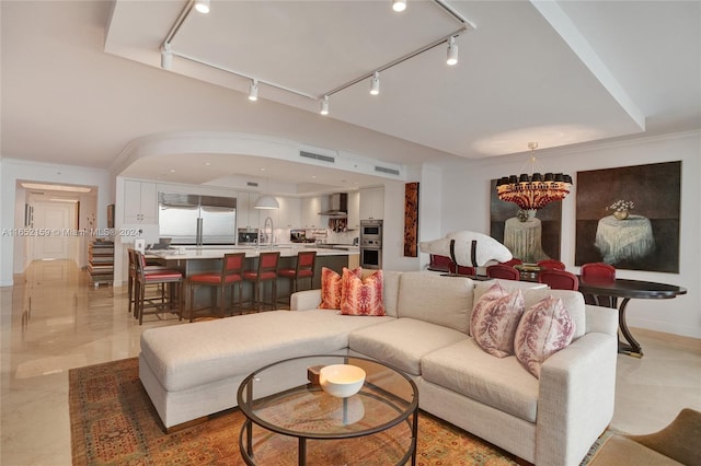 living room featuring track lighting, sink, crown molding, and a chandelier