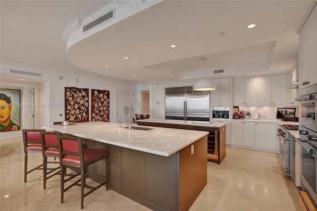 kitchen featuring sink, an island with sink, white cabinets, hanging light fixtures, and stainless steel appliances