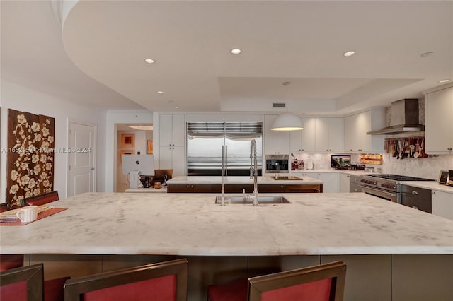 kitchen with hanging light fixtures, backsplash, wall chimney exhaust hood, high end appliances, and a breakfast bar area