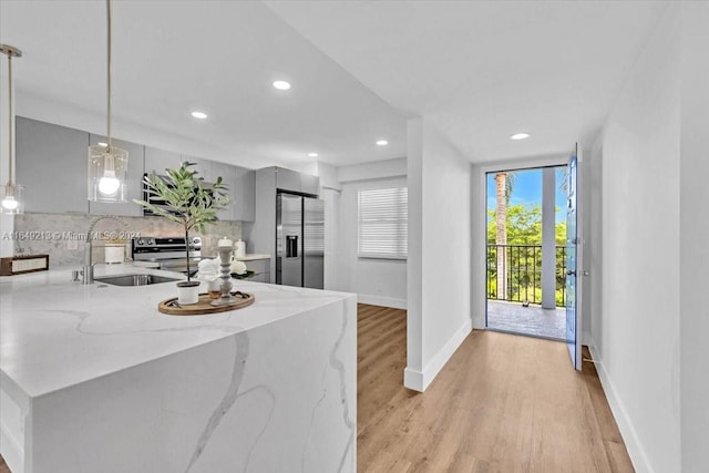 kitchen with sink, hanging light fixtures, light stone countertops, kitchen peninsula, and stainless steel appliances