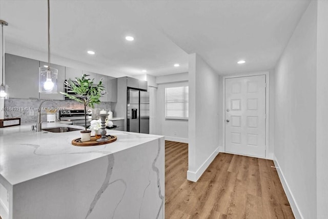 kitchen with sink, light hardwood / wood-style flooring, decorative light fixtures, light stone counters, and kitchen peninsula