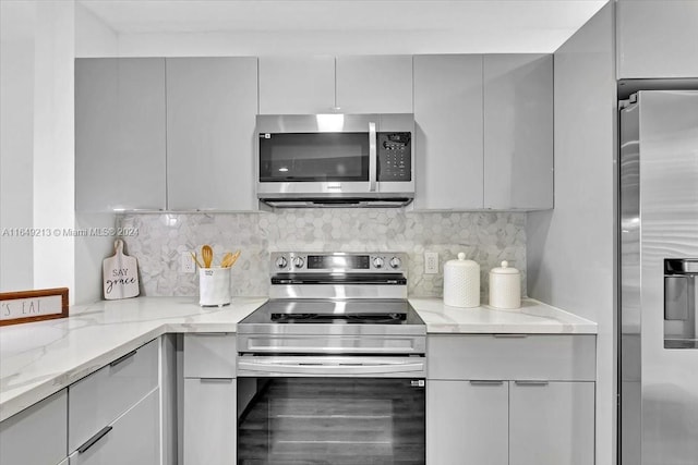 kitchen with gray cabinetry, light stone countertops, decorative backsplash, and appliances with stainless steel finishes