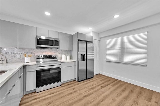 kitchen with gray cabinetry, decorative backsplash, light wood-type flooring, light stone counters, and stainless steel appliances