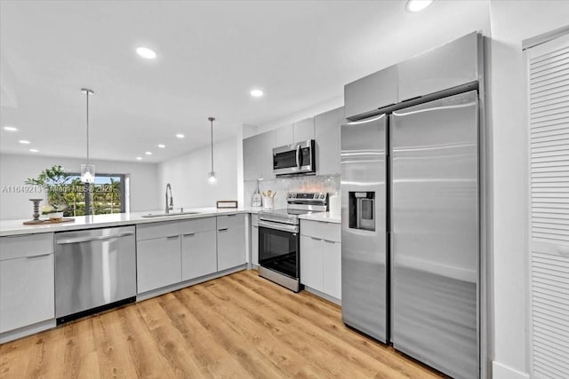 kitchen with decorative backsplash, appliances with stainless steel finishes, light wood-type flooring, sink, and pendant lighting