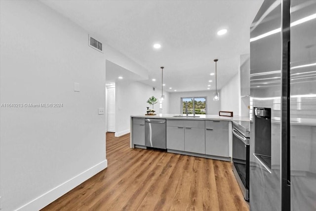 kitchen with kitchen peninsula, stainless steel appliances, sink, pendant lighting, and light hardwood / wood-style floors