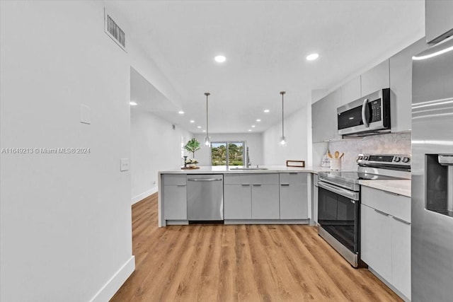 kitchen with hanging light fixtures, tasteful backsplash, kitchen peninsula, appliances with stainless steel finishes, and light wood-type flooring