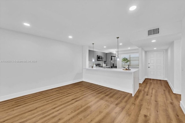 kitchen with kitchen peninsula, appliances with stainless steel finishes, tasteful backsplash, light hardwood / wood-style flooring, and hanging light fixtures