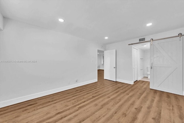 unfurnished bedroom with a barn door and light hardwood / wood-style floors