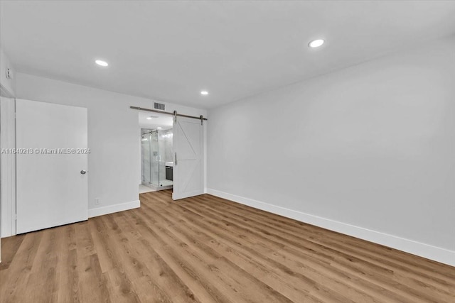 unfurnished bedroom featuring a barn door, ensuite bathroom, and light hardwood / wood-style flooring