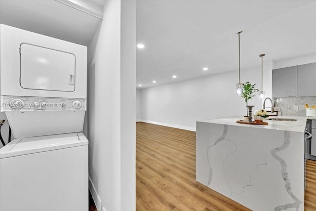 clothes washing area with light hardwood / wood-style flooring, stacked washer / dryer, and sink