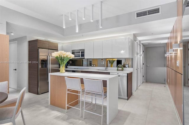 kitchen with white cabinets, stainless steel appliances, sink, a breakfast bar area, and a kitchen island