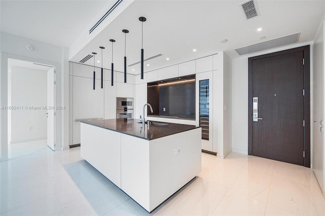 kitchen with sink, an island with sink, white cabinets, and hanging light fixtures