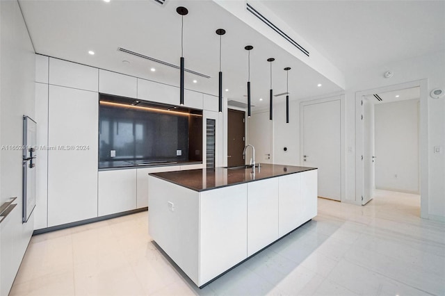 kitchen with white cabinets, hanging light fixtures, sink, black electric cooktop, and a center island with sink