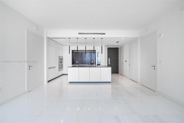 kitchen with decorative light fixtures, an island with sink, white cabinetry, and sink