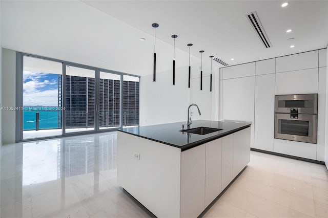 kitchen with stainless steel double oven, decorative light fixtures, sink, a center island with sink, and white cabinets