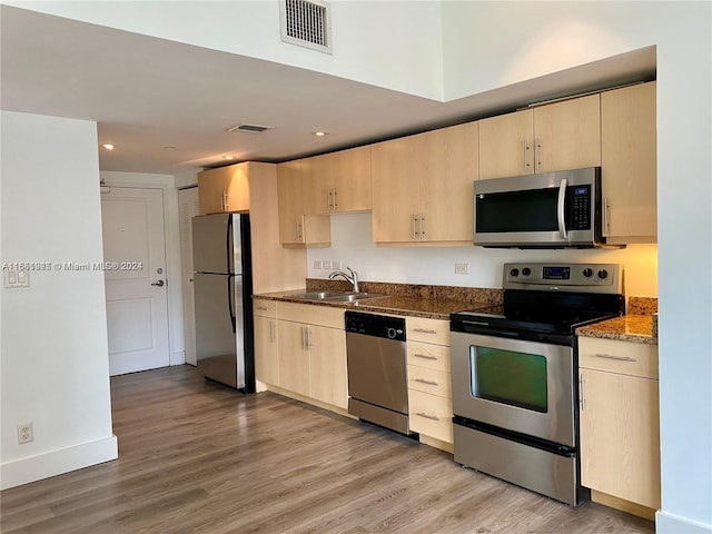 kitchen featuring dark stone countertops, stainless steel appliances, light hardwood / wood-style floors, sink, and light brown cabinets