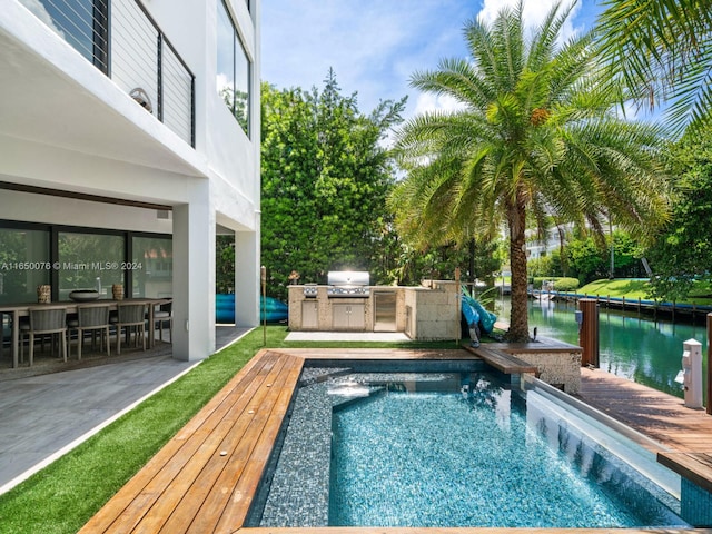 view of pool with grilling area, a water view, an outdoor kitchen, and a patio area