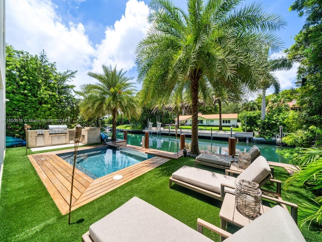 view of pool with a water view, an outdoor kitchen, area for grilling, and a yard