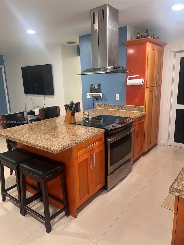 kitchen with wall chimney exhaust hood, stainless steel electric stove, a breakfast bar, light stone countertops, and light tile patterned floors