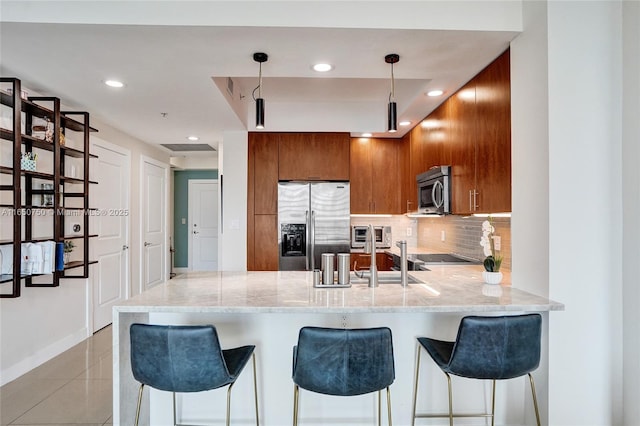 kitchen featuring stainless steel appliances, hanging light fixtures, backsplash, a peninsula, and a kitchen bar