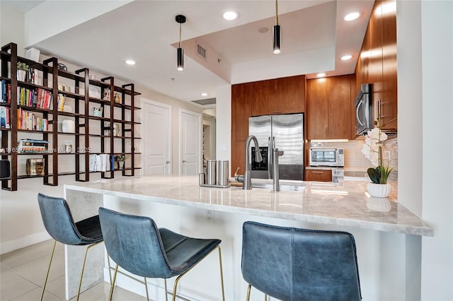 kitchen featuring visible vents, decorative backsplash, a peninsula, stainless steel appliances, and pendant lighting