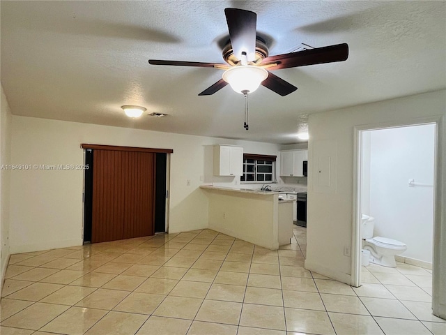 kitchen featuring a textured ceiling, light tile patterned floors, kitchen peninsula, ceiling fan, and white cabinets