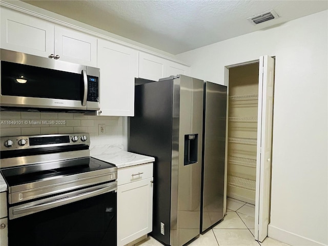 kitchen with light tile patterned flooring, white cabinetry, decorative backsplash, light stone counters, and stainless steel appliances