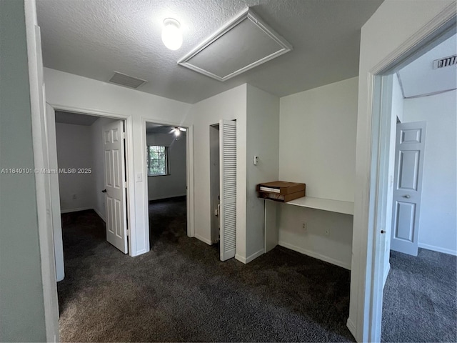 corridor featuring a textured ceiling and dark colored carpet