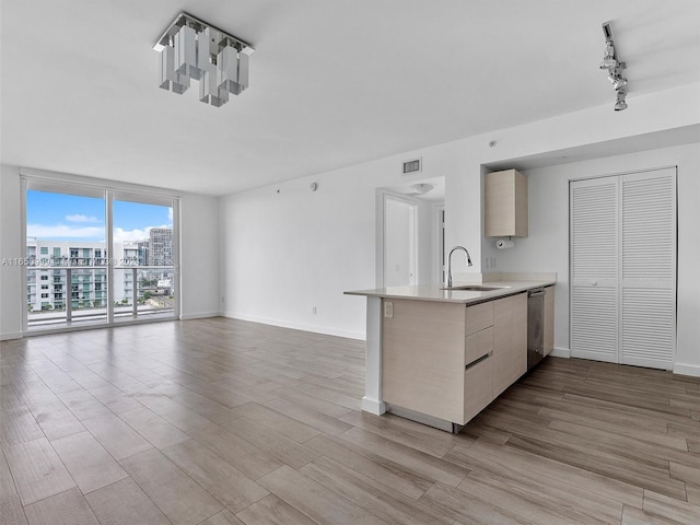 kitchen featuring sink, kitchen peninsula, stainless steel dishwasher, light brown cabinetry, and light hardwood / wood-style floors