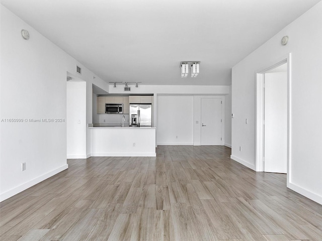 unfurnished living room with light wood-type flooring, rail lighting, and sink