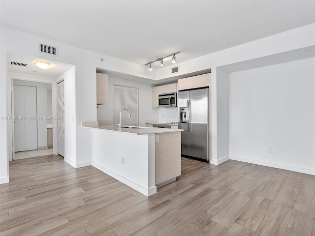 kitchen with appliances with stainless steel finishes, kitchen peninsula, light wood-type flooring, track lighting, and sink