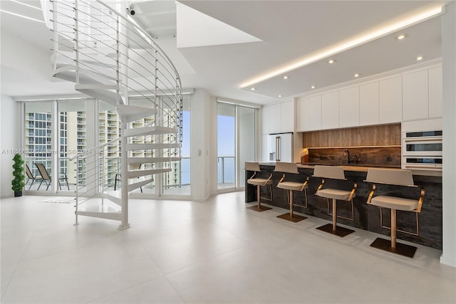 kitchen with double oven, high end white fridge, white cabinetry, and sink